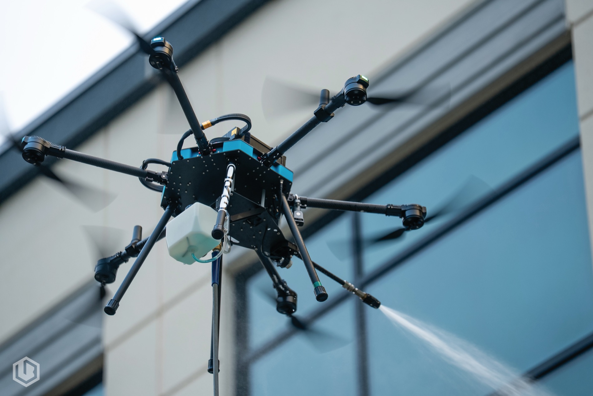 A cleaning drone rinsing a glass elevation, water sheeting off the panes