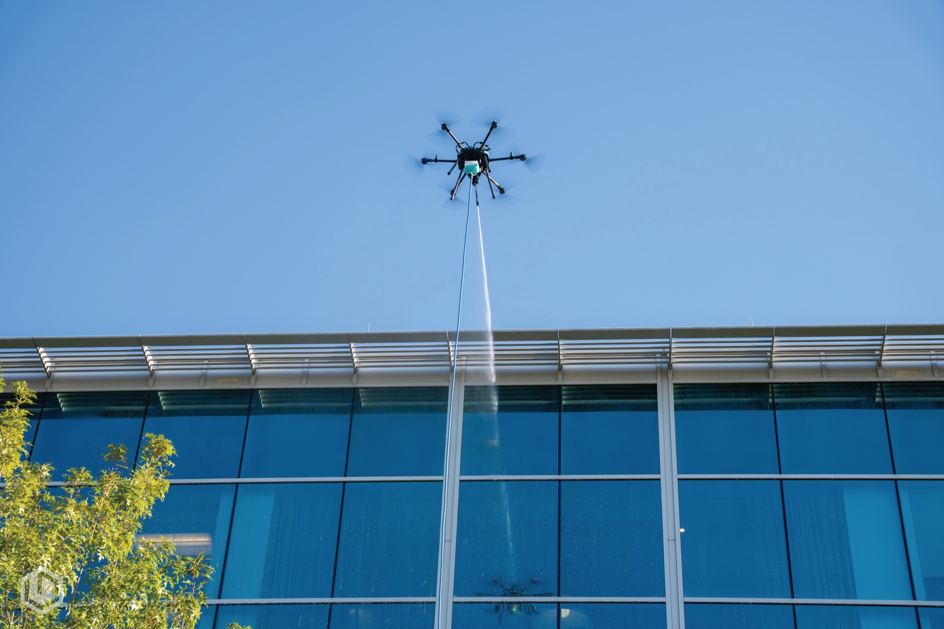 A Lucid Bots Sherpa cleaning drone spraying the glass elevation of an office building