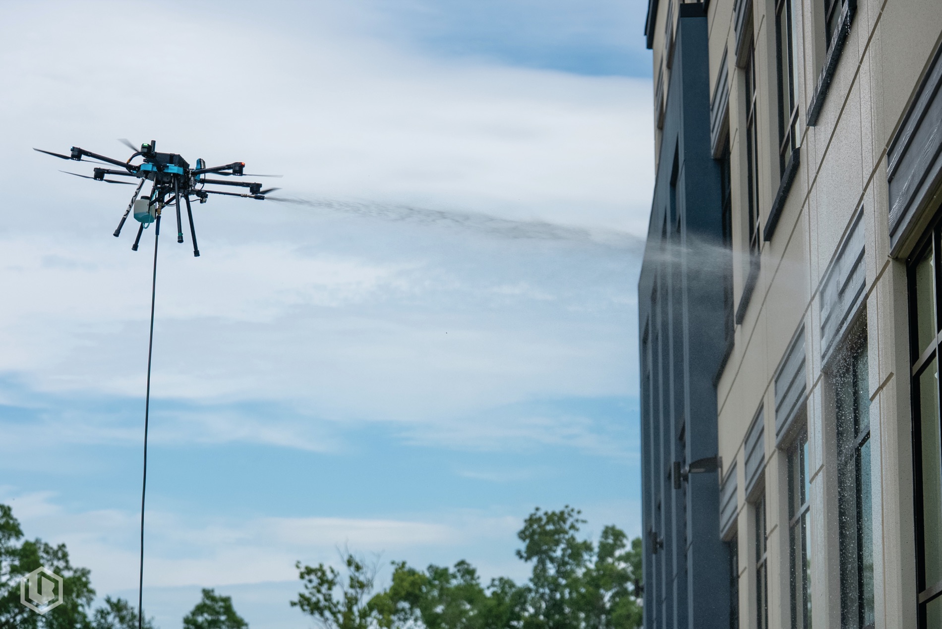 A cleaning drone spraying a building facade, supply hose running to the ground unit