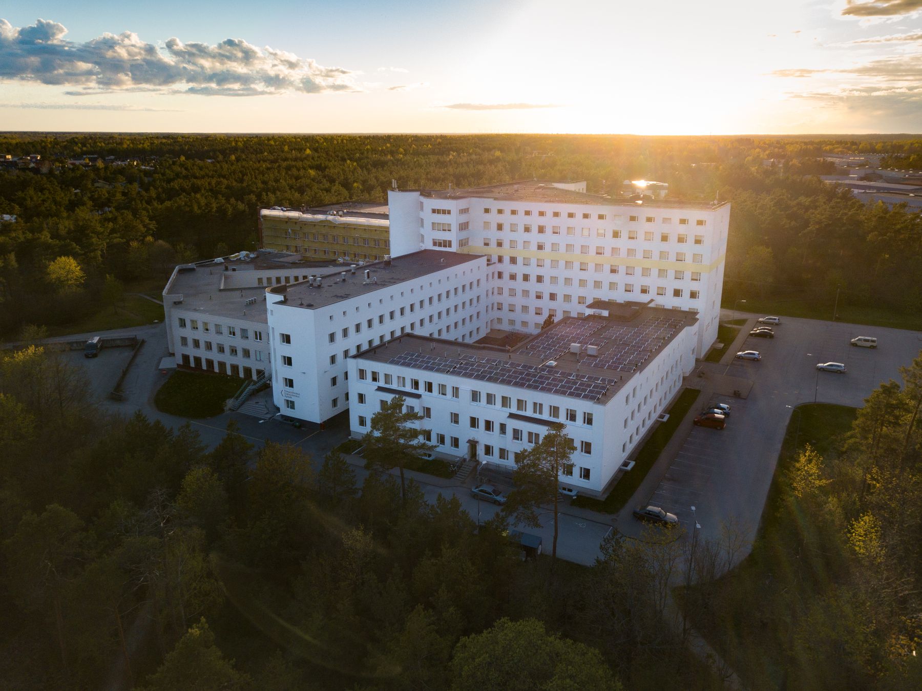 Aerial view of a modern hospital building surrounded by trees at sunset