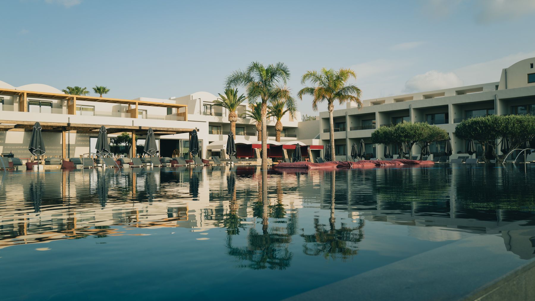 Resort hotel exterior with balconied guest wings and palm trees reflected in the pool