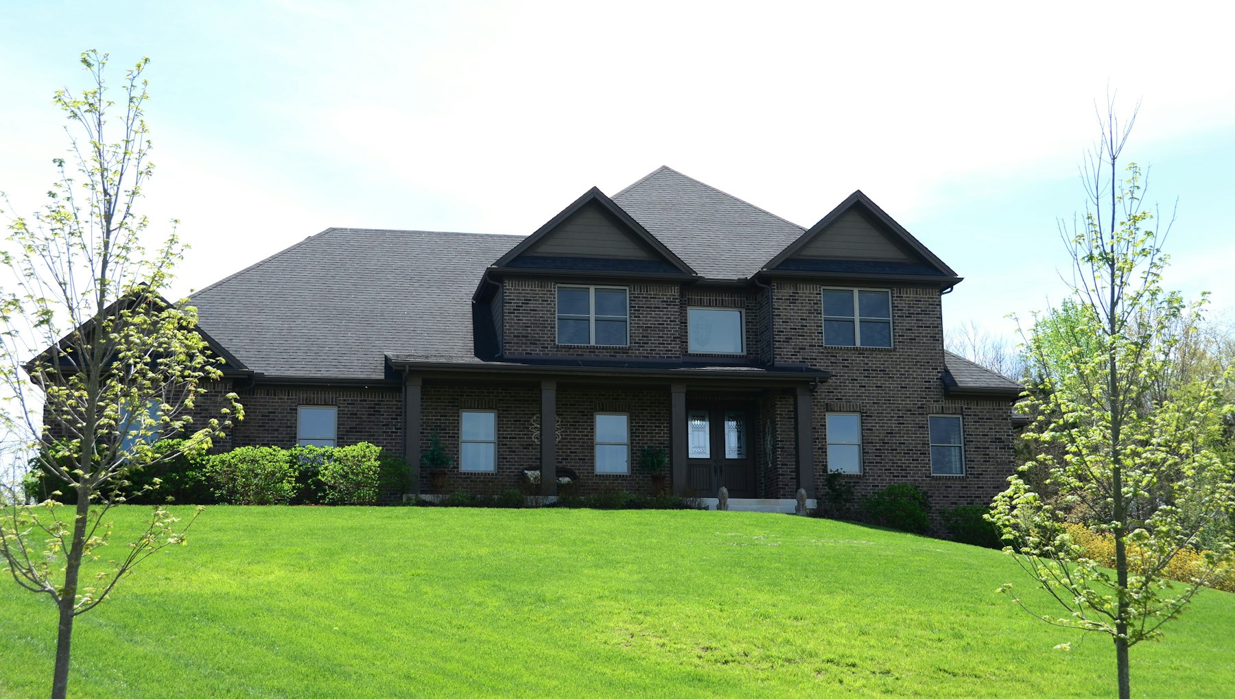Large brick two-story American suburban single-family home with a landscaped lawn
